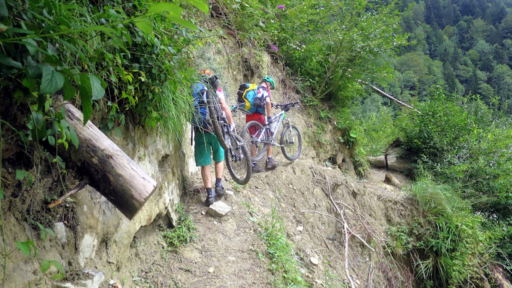 zwei Mountainbiker tragen ihre Räder an einer schmalen Passage -Transalp vom Bodensee zum Comer See