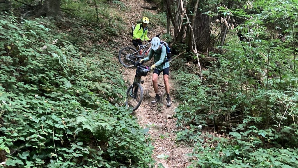 Mountainbiker schieben ihre Räder bei der Monviso Rundtour einen Steilen Trail hinunter